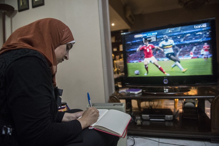Football analyst Manar Sarhan takes notes as she watches the Euro 2016 quarter-final between Wales and Belgium at her home in the Egyptian capital Cairo on July 1, 2016. The 27-year-old woman who works as a dentist at a government medical centre appears weekly on the private CBC television channel to comment on matches in the competition, a rare sight in a field monopolised by former football players, all of them men. / AFP PHOTO / KHALED DESOUKI / TO GO WITH AFP STORY BY HAITHAM EL-TABEI