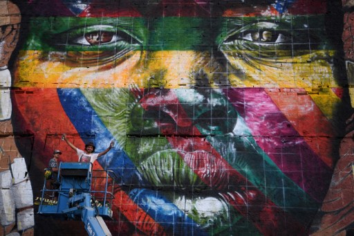 Brazilian artist Eduardo Kobra stands next to his huge mural representing the five continents, at the Olympic Boulevard, in Rio de Janeiro, Brazil, on July 14, 2016. / AFP PHOTO / CHRISTOPHE SIMON