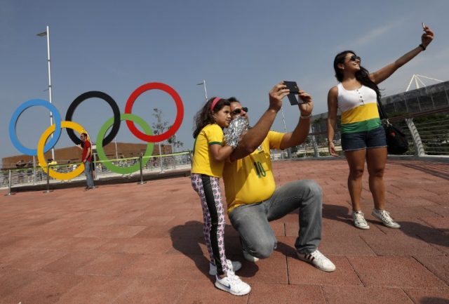 Visitors pose for a photograph beside the Olympic Rings in the Olympic Park during the Rio 2016 Olympic Games in Rio de Janeiro on August 9, 2016.   / AFP PHOTO / ADRIAN DENNIS