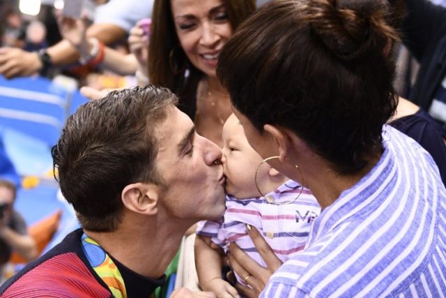 USA's Michael Phelps (L) kisses his son Boomer next to his partner Nicole Johnson after he won the Men's 200m Butterfly Final during the swimming event at the Rio 2016 Olympic Games at the Olympic Aquatics Stadium in Rio de Janeiro on August 9, 2016.   / AFP PHOTO / Martin BUREAU