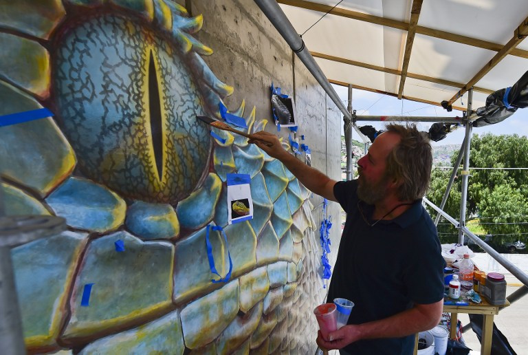 US artist John Pugh paint a mural at a poor neighborhood in Ecatepec, Mexico on August 25, 2016.  Dozens of murals were painted on buildings in a poor neighborhood in Ecatepec, on the route of a new cable car that will run this year. / AFP PHOTO / RONALDO SCHEMIDT / TO GO WITH AFP STORY BY JENNIFER GONZALEZ