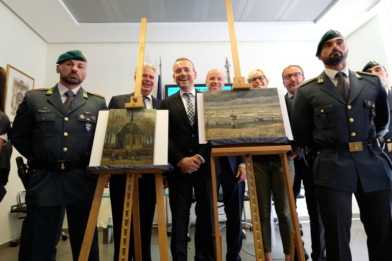Axel Ruger (C), Director of the Van Gogh museum poses next to Congregation Leaving the Reformed Church in Nuenen" (L) and "The Beach At Scheveningen During A Storm" (R) by Vincent van Gogh, two Van Gogh paintings stolen in Amsterdam 14 years ago and recently recovered by organised crime investigators in Italy, on September 30, 2016. 