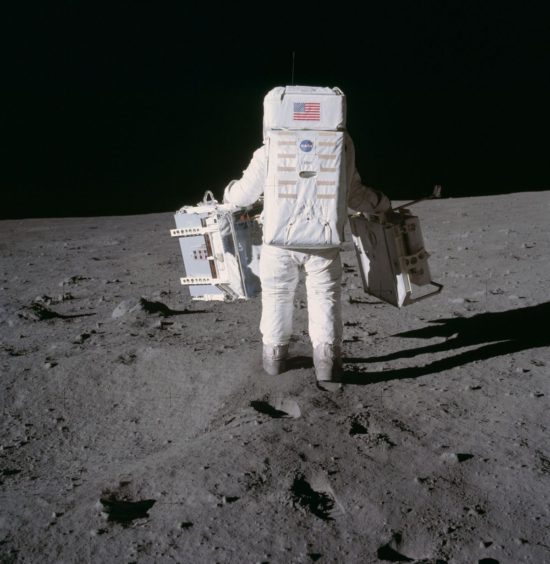 Buzz Aldrin se mueve hacia la posición donde desplegará dos componentes del Paquete de Primeros Experimentos Científicos Apollo en la superficie de la Luna durante la misión. 