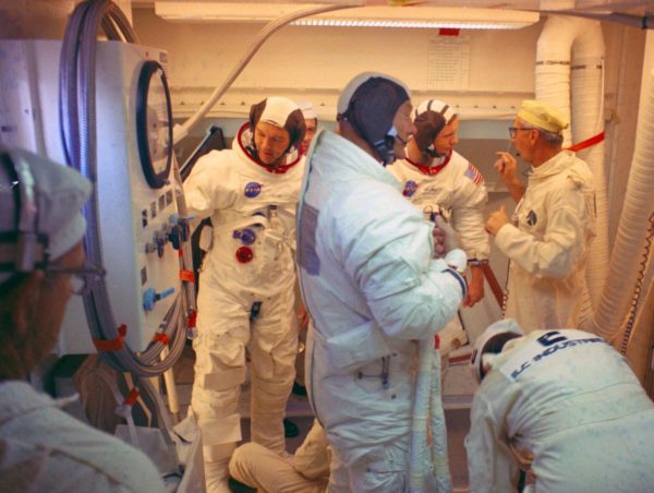 Dentro de la "Habitación Blanca" en la cima del Complejo de Lanzamiento 39, Plataforma A, los astronautas del Apollo 11 se retiran del lugar luego de participar en una demostración de cuenta regresiva. Al frente se puede observar al astronauta Buzz Aldrin, mientras que atrás se puede ver a Armstrong intercambiando palabras con el líder Guenter Wendt. 