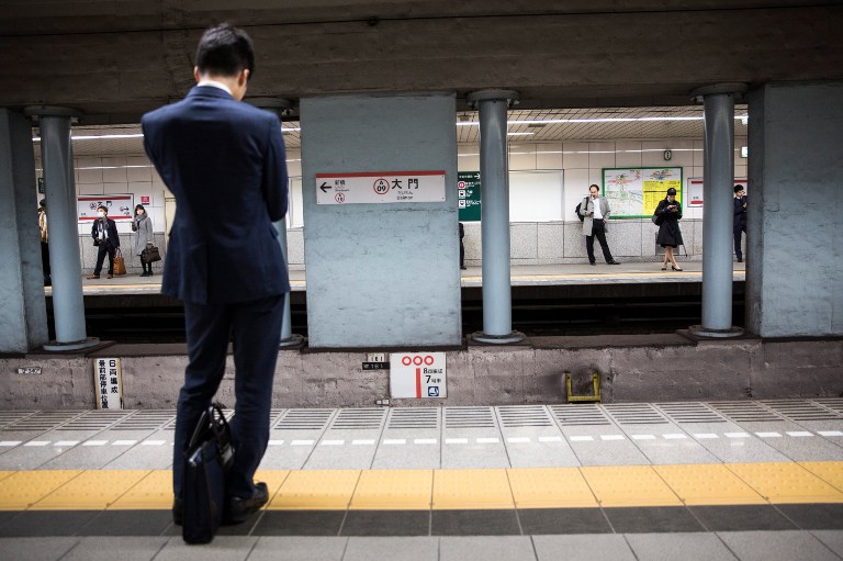 Commuters wait for the train at a subway station in central Tokyo on December 27, 2016.  Japan's consumer prices fell for the ninth straight month in November, official data showed on December 27, while household spending declined and unemployment ticked up.  / AFP PHOTO / Behrouz MEHRI
