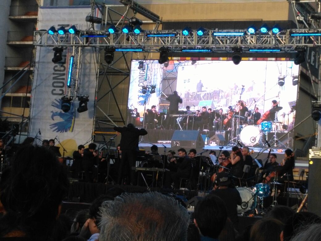 Orquesta ejecuta concierto frente a espectadores en escenario instalado frente a Tribunales penquistas