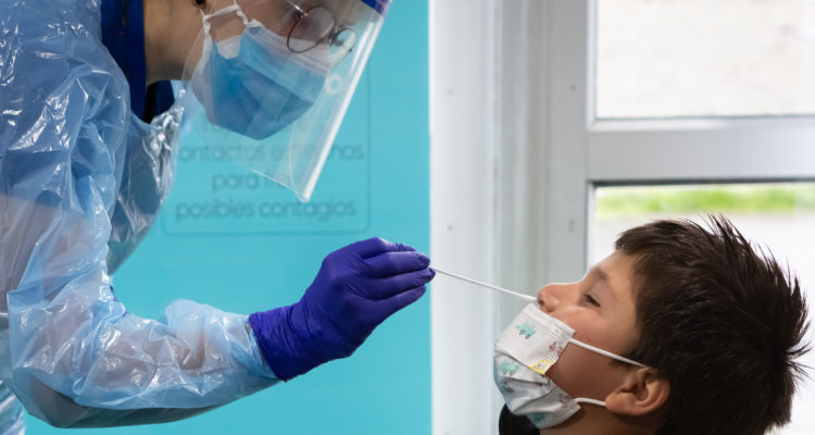 Una mujer contraje, guantes, mascarilla y mascara facial aplica un test PCR a niño escolar en Puerto Montt | Felipe Constanzo, Agencia UNO. 