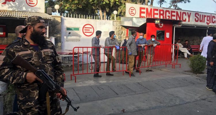 A Taliban fighter (L) stands guard as Afghan medical staff members wait at the entrance of a hospital to receive the victims of an explosion in Kabul on October 3, 2021 | Agence France-Presse