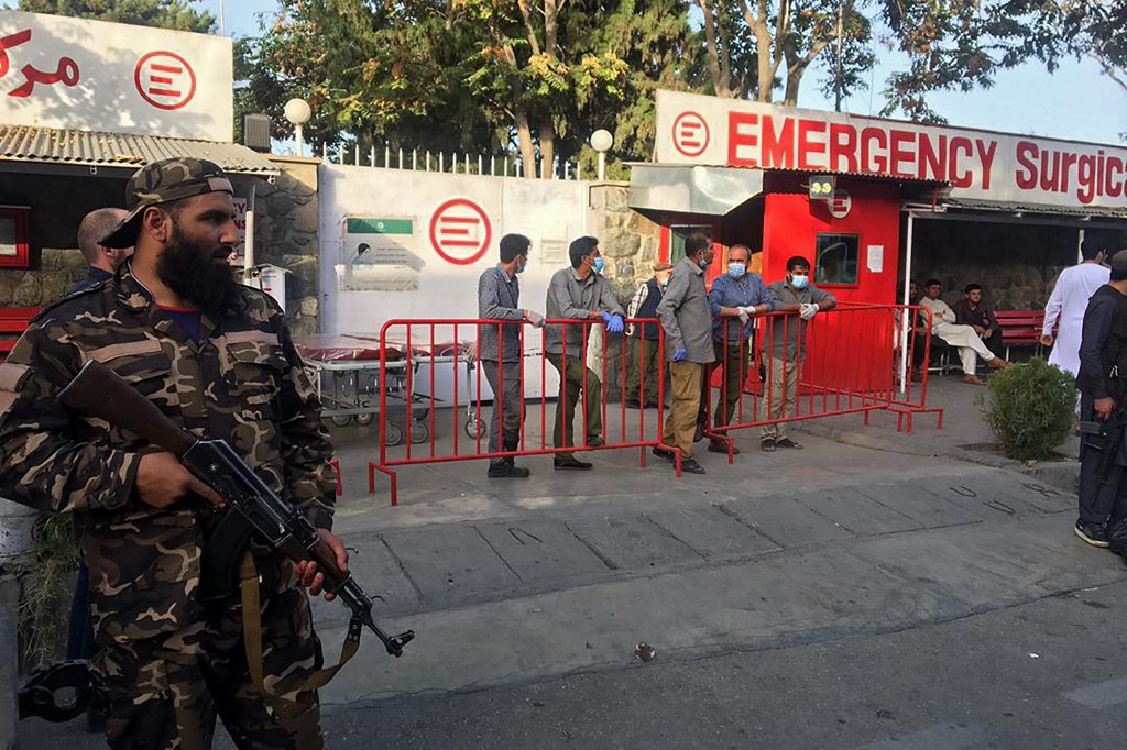 A Taliban fighter (L) stands guard as Afghan medical staff members wait at the entrance of a hospital to receive the victims of an explosion in Kabul on October 3, 2021 | Agence France-Presse