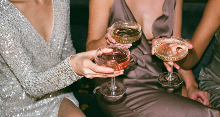 En la foto, tres mujeres chocan copas con alcohol en un brindis.