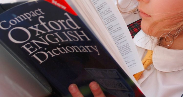 Niña lee el diccionario de Oxford.