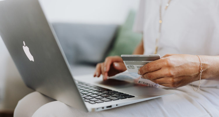 Una mujer tiene un notebook en sus piernas y una tarjeta de crédito en su mano, en señal de que está comprando por internet en el Black Friday.