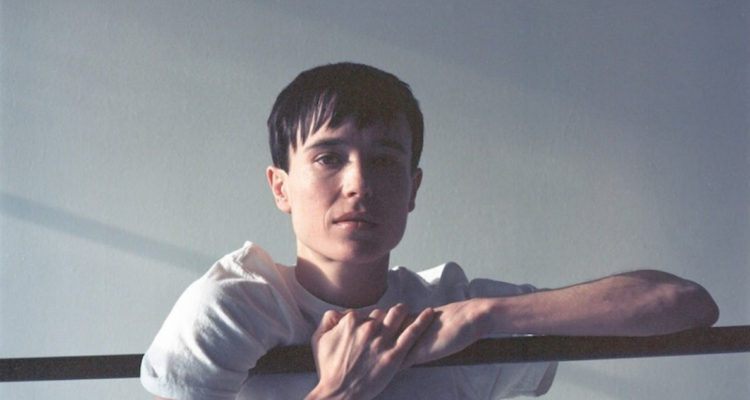 Elliot Page aparece sostenido de un fierro y mira serio a la cámara.