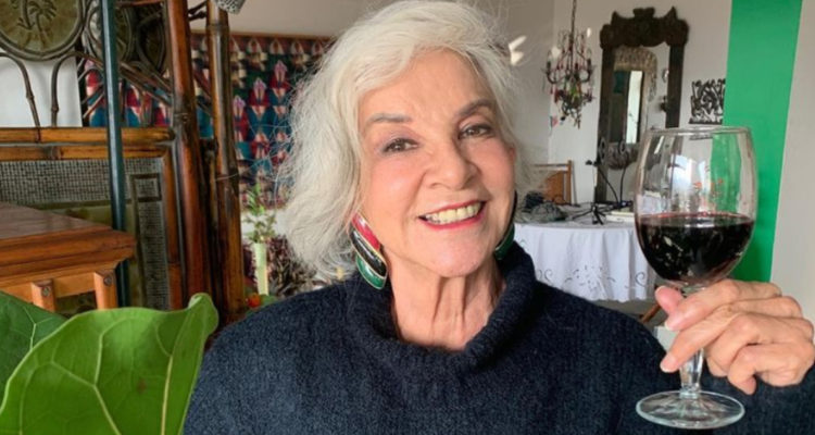 La actriz aparece en su hogar mientras sonríe y sostiene una copa de vino.