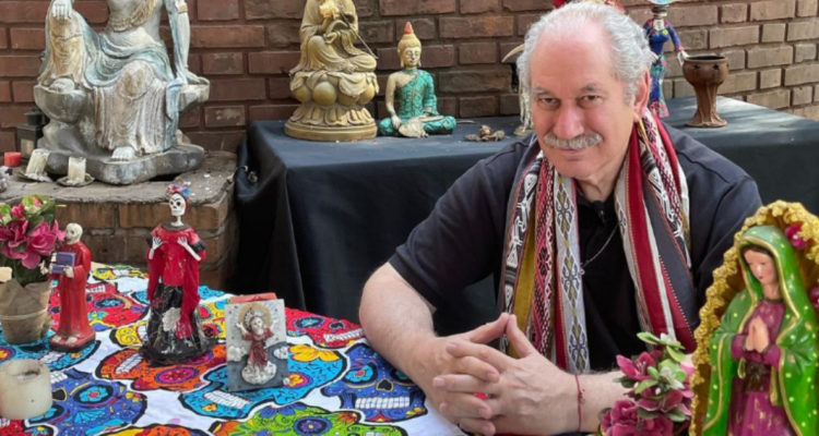 El tarotista Pedro engel sonríe a la camara sentado en una nesón con esculturas y talismanes.