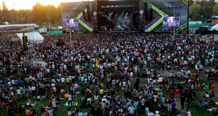 En la imagen se ve a un miles de personas sentadas alrededor de uno de los escenarios del festival musical Lollapalooza.