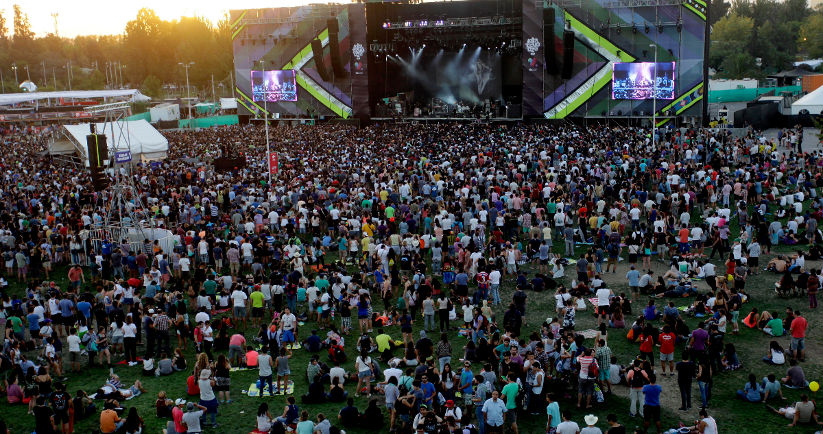 En la imagen se ve a un miles de personas sentadas alrededor de uno de los escenarios del festival musical Lollapalooza.