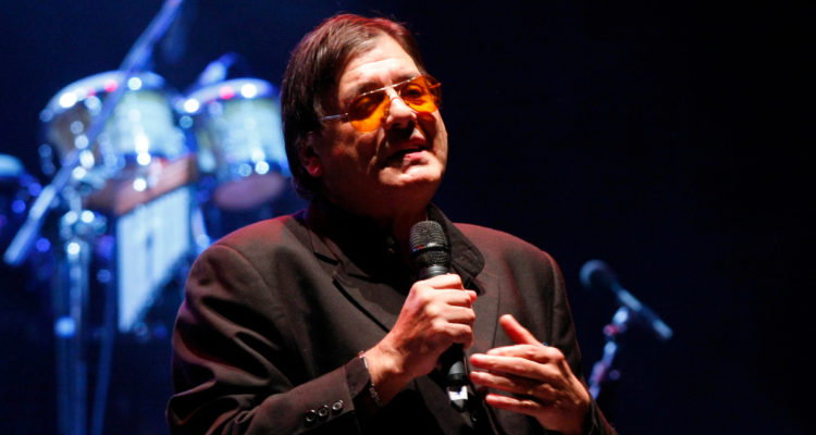 El cantante aparece cantando en un escenario.