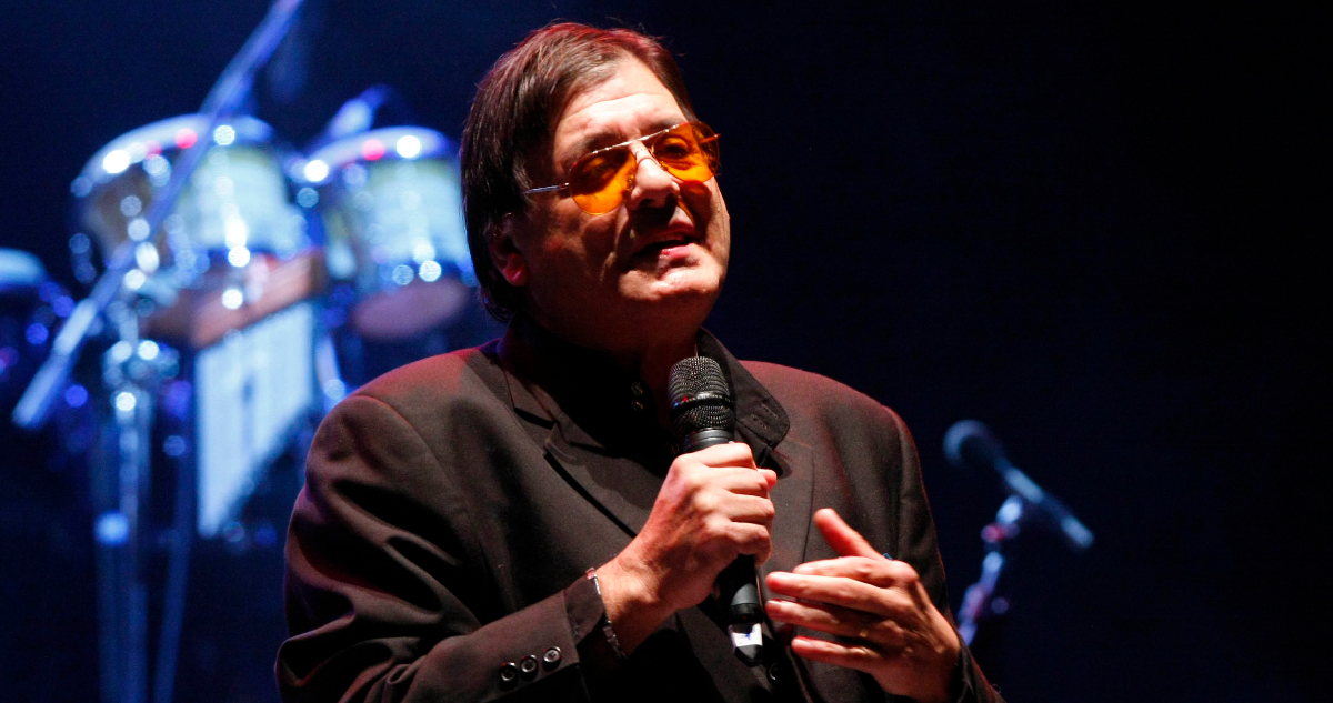 El cantante aparece cantando en un escenario.