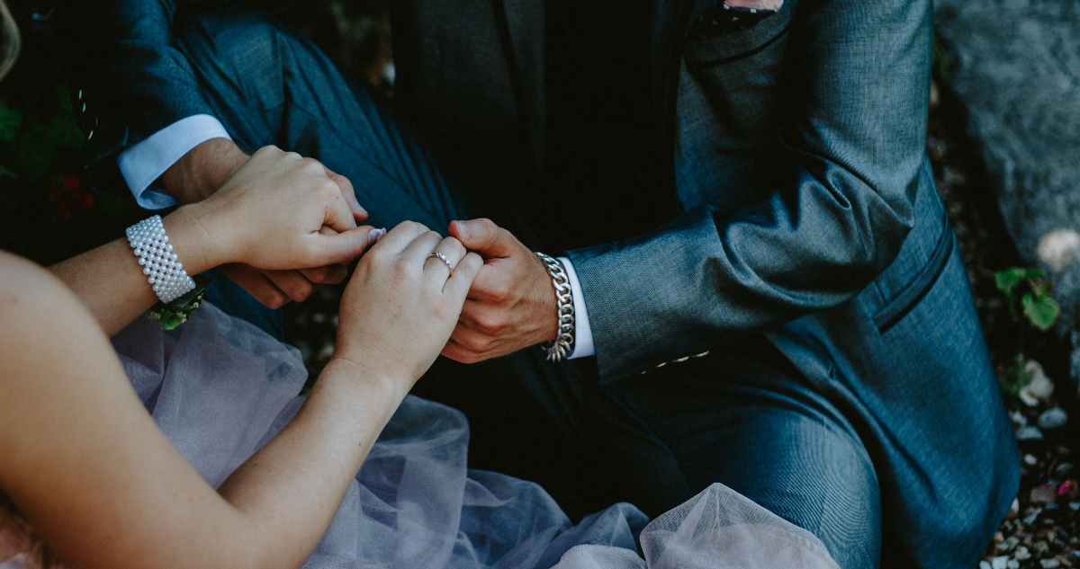 En la foto, un hombre y una mujer aparecen sostenidas de la mano. LLevan un aniñño de bodas y están vestidos para la ocasión.