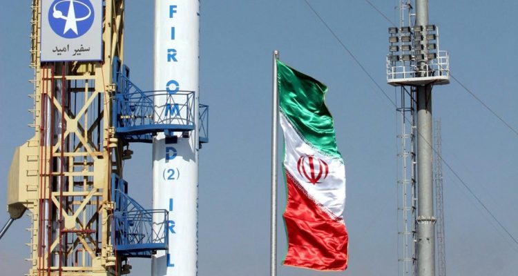 Un cohete junto a una bandera iraní en una plataforma de despegue.