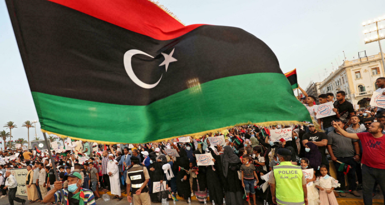 Una bandera libia flameando frente a manifestantes.