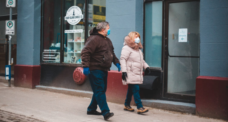 Un hombre y una mujer caminando por la calle mientras utilizan mascarillas.
