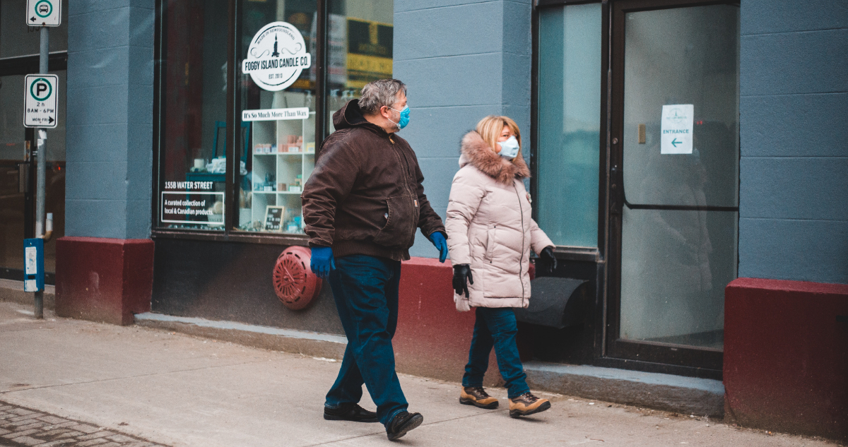 Un hombre y una mujer caminando por la calle mientras utilizan mascarillas.