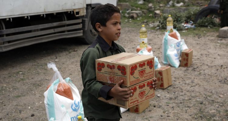 Un niño cargando una caja de comida del programa de alimentación de la ONU.