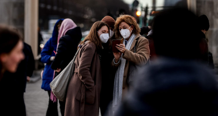 Dos mujeres ven su telefono mientras usan mascarillas por la nueva variante del covid-19, Ómicron.