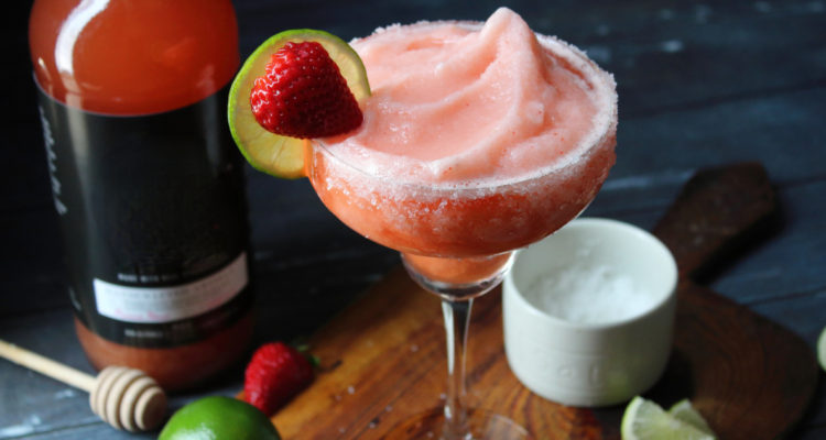 En la foto se puede observar una copa con frutilla sour. La copa está adornada con limón, azúcar y frutilla.