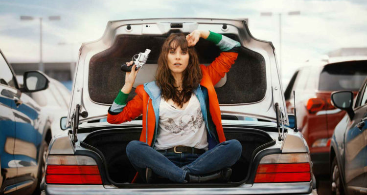 Barbara, protagonista de Express, con un arma en su mano a la vez que está sentada en la cajuela de un automovil.