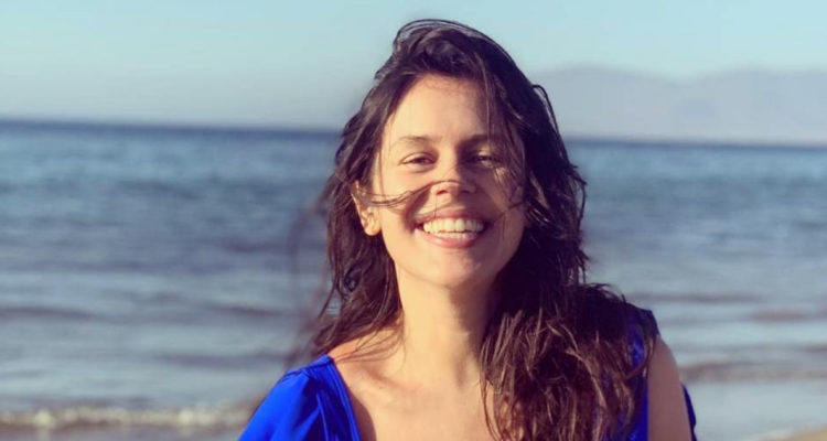 La actriz Carola Varleta sonriendo a la cámara en una playa.