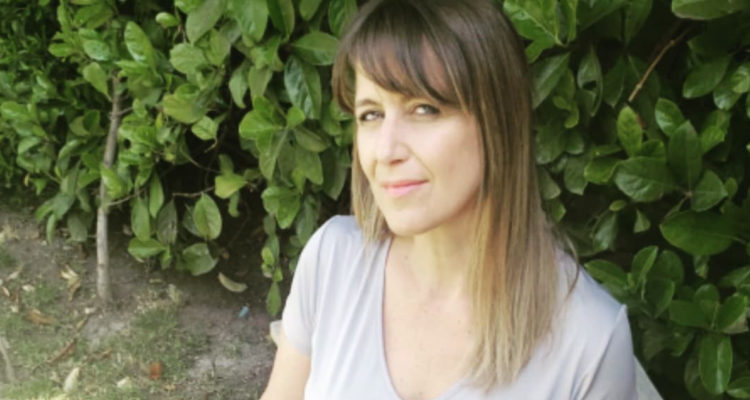 La periodista Carolina Urrajola sentada en un patio, sonríe levemente.