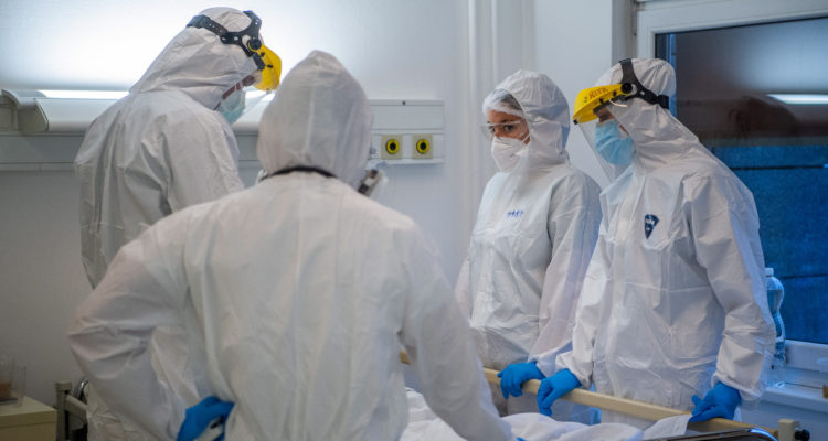 En la fotografía se ven a cuatro funcionarios de la salud completamente cubiertos con overoles, mascarillas y protectores faciales parados alrededor de una camilla. La imagen da a entender su protección ante el coronavirus y sus mutaciones, como la variante Delta, en hospitales.