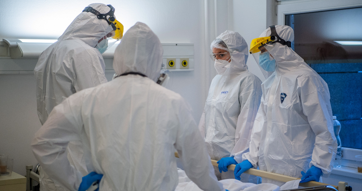 En la fotografía se ven a cuatro funcionarios de la salud completamente cubiertos con overoles, mascarillas y protectores faciales parados alrededor de una camilla. La imagen da a entender su protección ante el coronavirus y sus mutaciones, como la variante Delta, en hospitales.