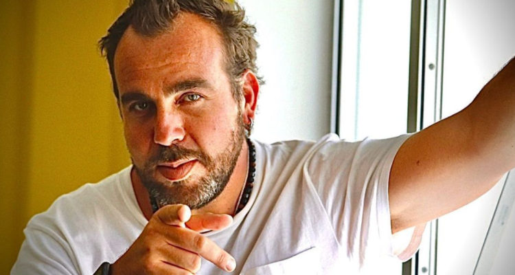 El presentador de televisión Francisco Kaminski apoyándose en un muro a la vez que con el otro brazo apunta a la cámara.