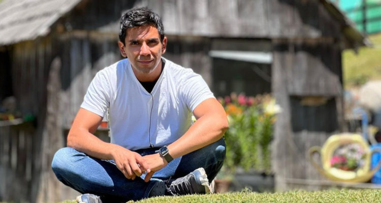 El periodista Juan Pablo Queraltó sentado con las piernas cruzadas en medio del antejardín de una cabaña.