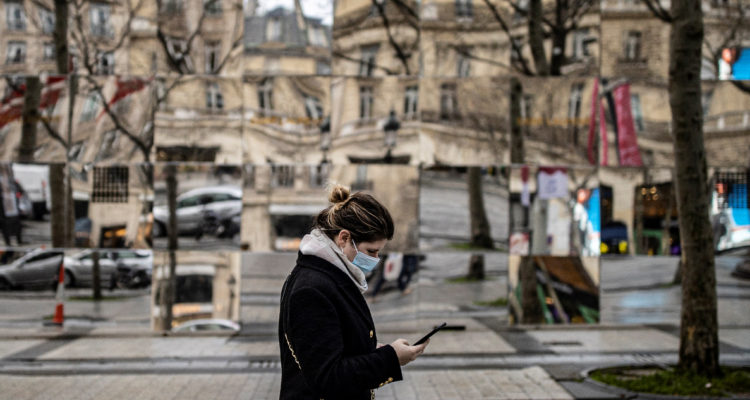 Una mujer camina por la vía pública mirando su celular, a la vez que lleva una mascarilla ante la ola de contagios por Ómicron.