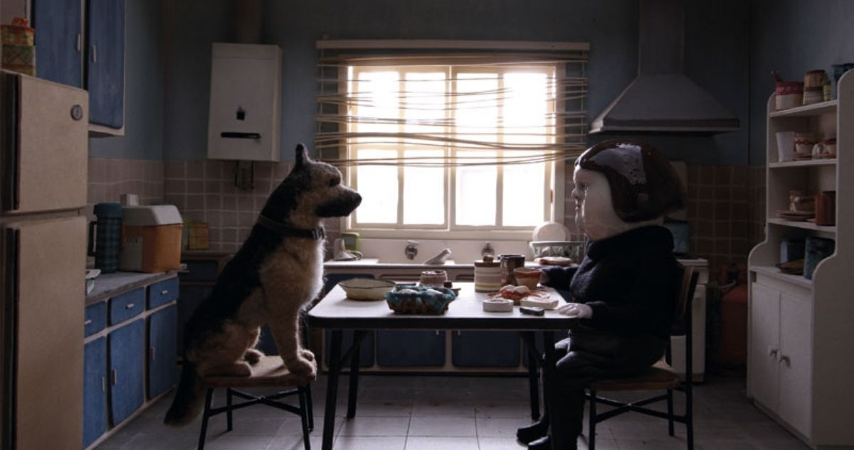 En la imagen se ve a un perro y la protagonista del cortometraje. Ambos están sentados en una mesa, comiendo.
