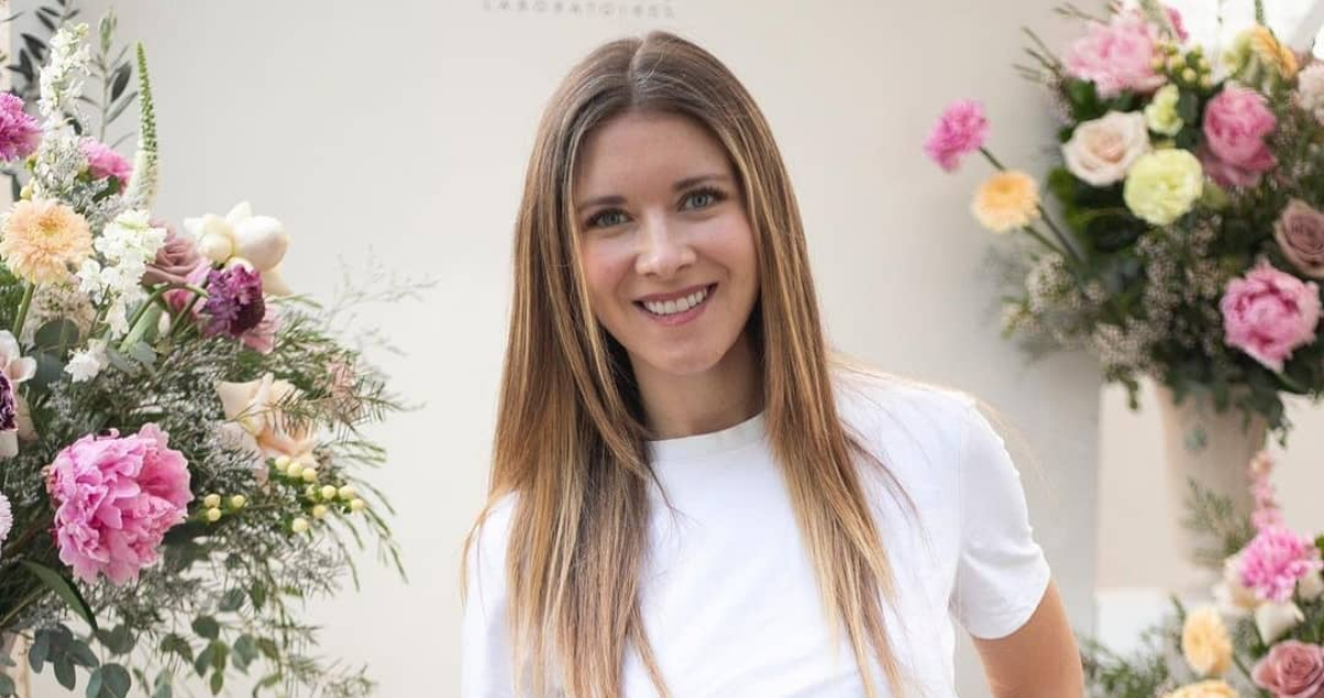 La animadora Carla Jara sonriendo a la cámara mientras se encuentra rodeada de flores rosadas. La actriz descartó volver a bailar a Mekano.
