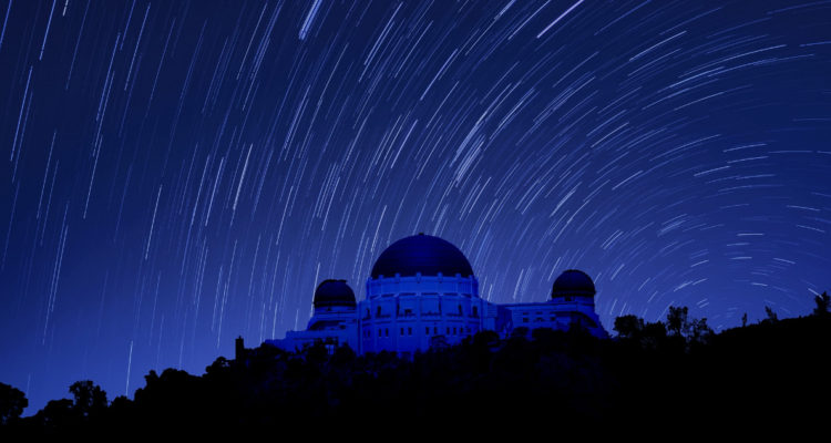 En la imagen se ve un edificio de un observatorio en medio de la noche. Se ven diferentes estrellas pasando sobre el inmueble.