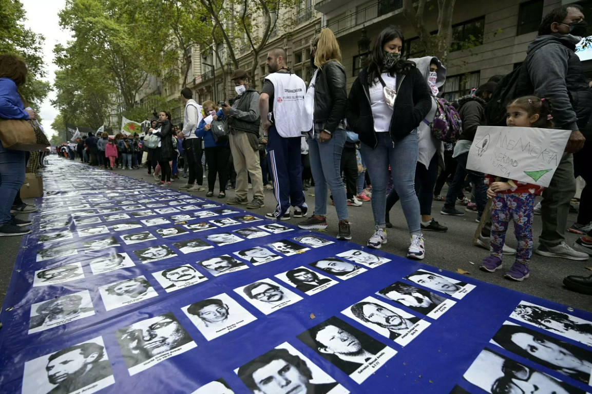 Una niña (D) sostiene una pancarta que dice "Memoria, Verdad, Justicia" junto a una gran pancarta con retratos de personas desaparecidas durante la dictadura militar (1976-1983).
