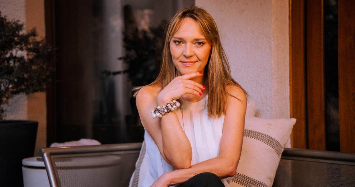 Carola Brethauer aparece sentada en un sofá con las pernas cruzadas. Apoya su rostro en su mano izquierda mientras da una sonrisa leve.