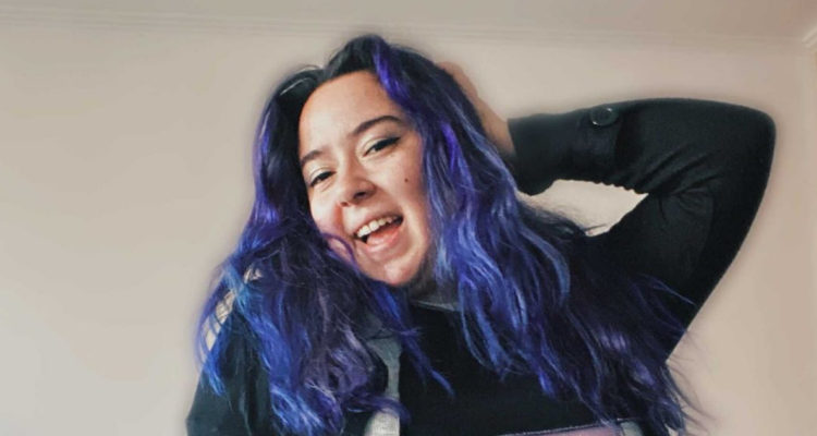 La exchica Rojo Christell sonriendo a la cámara mientras posa. La cantante se ha referido al bullying y el autoestima durante sus apariciones en pantalla.