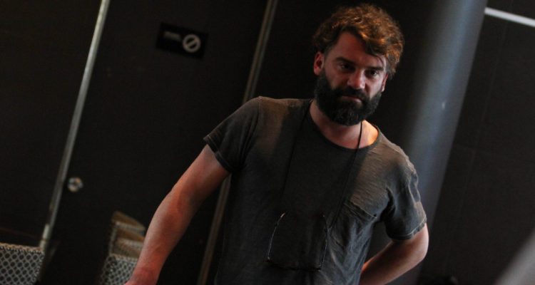 El actor Diego Muñoz usando una gran barba, mientras mira serio a las cámaras.