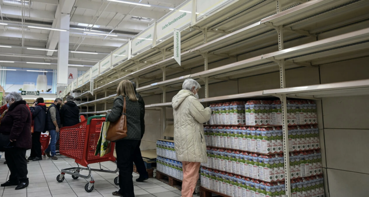 Unos clientes compran leche en un supermercado de Madrid con las estanterías vacías.