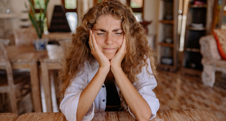 Una mujer apoya su cabeza en sus manos mientras se ve afligida pensando. La pérdida de memoria y concentración parecen ser un nuevo signo del COVID prolongado.