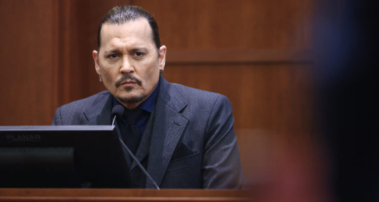 El actor Johnny Depp sentado serio en el estrado mientras escucha audios con la evidencia.