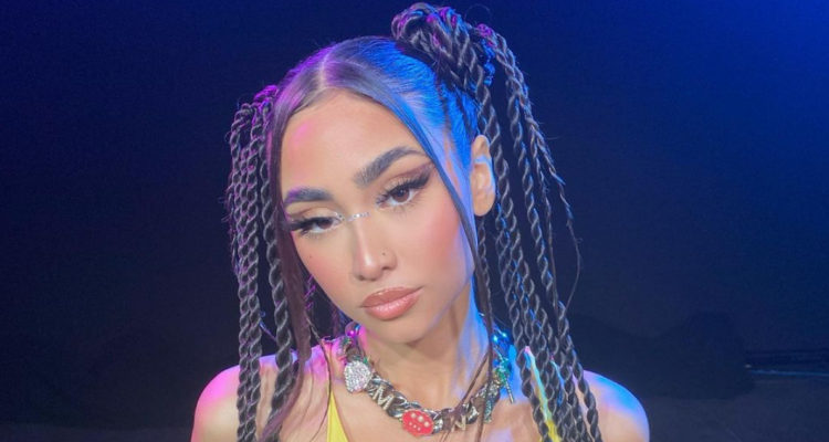 La cantante Paloma Mami tiene los brazos en la espalda y la cabeza levemente inclinada, mientras muestra una media sonrisa.